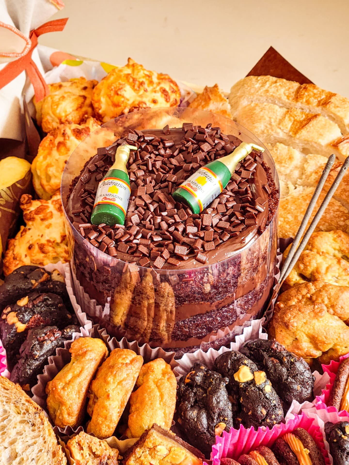 Detalhe do naked cake de chocolate com velas, cercado de pães de queijo