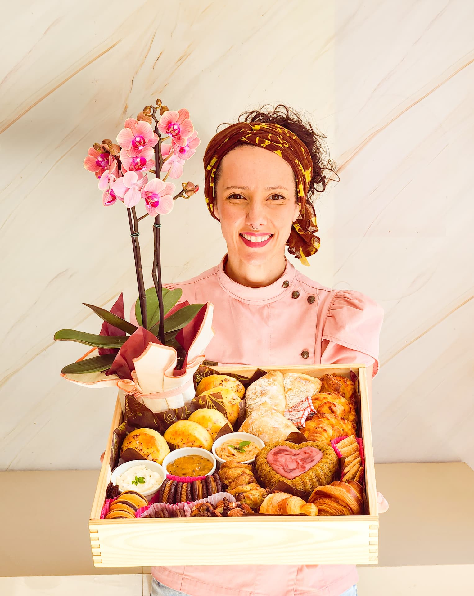 Caixa de madeira pinus aberta, cheia de pães, biscoitos e uma orquídea, sendo segurada